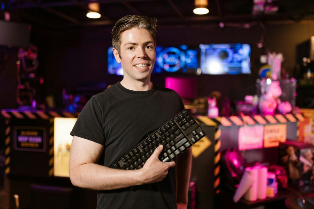 A cheerful man with a mechanical keyboard in a vibrant gaming environment.